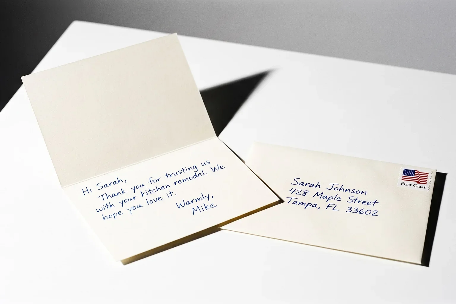 An open cream card with a thank-you note written in blue ballpoint pen, next to its hand-addressed envelope with a First Class stamp.